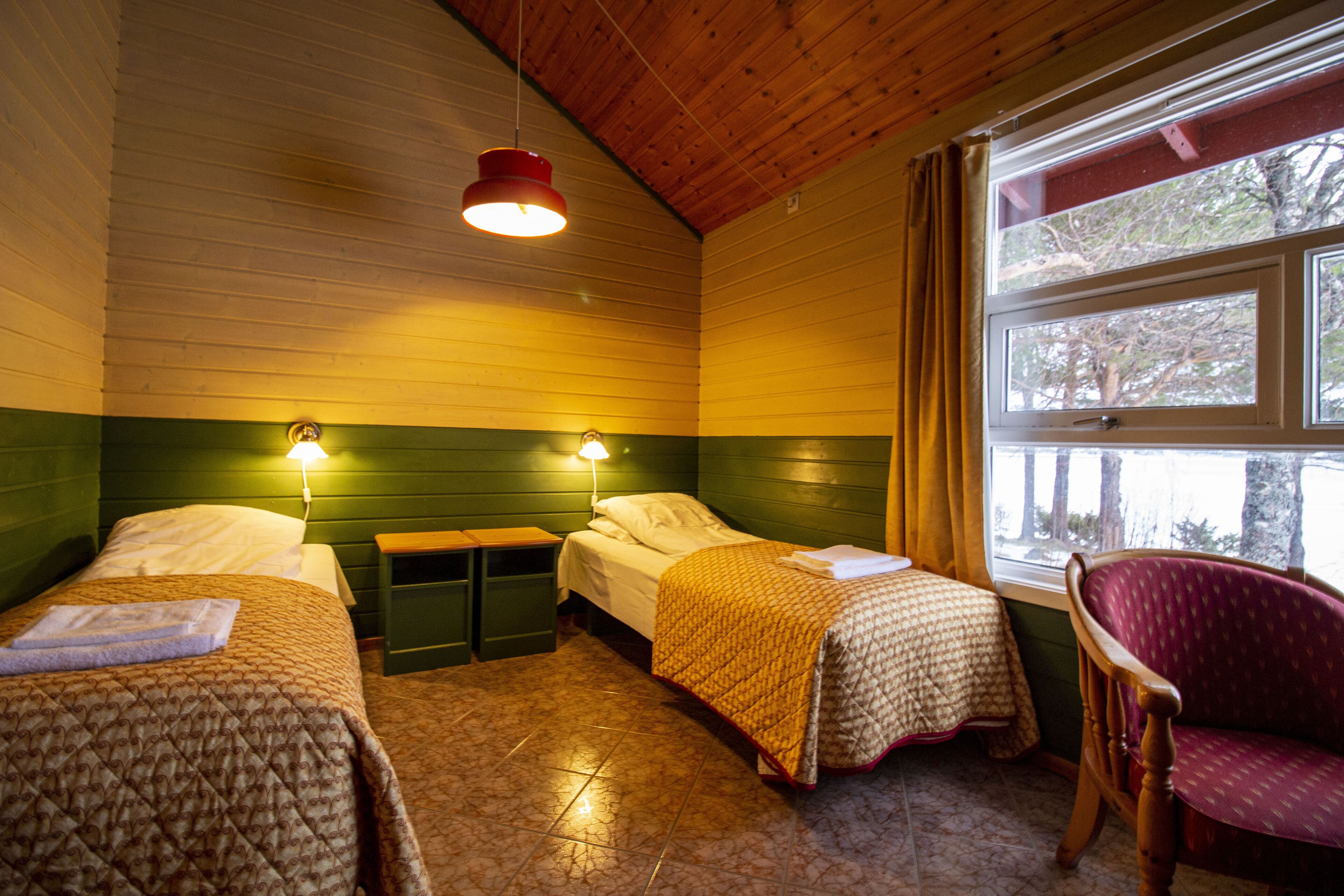A room with two beds, a chair, and a window with a view of trees.