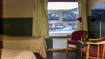 Een kamer met twee bedden, een stoel, een tafel en een raam met gordijnen.