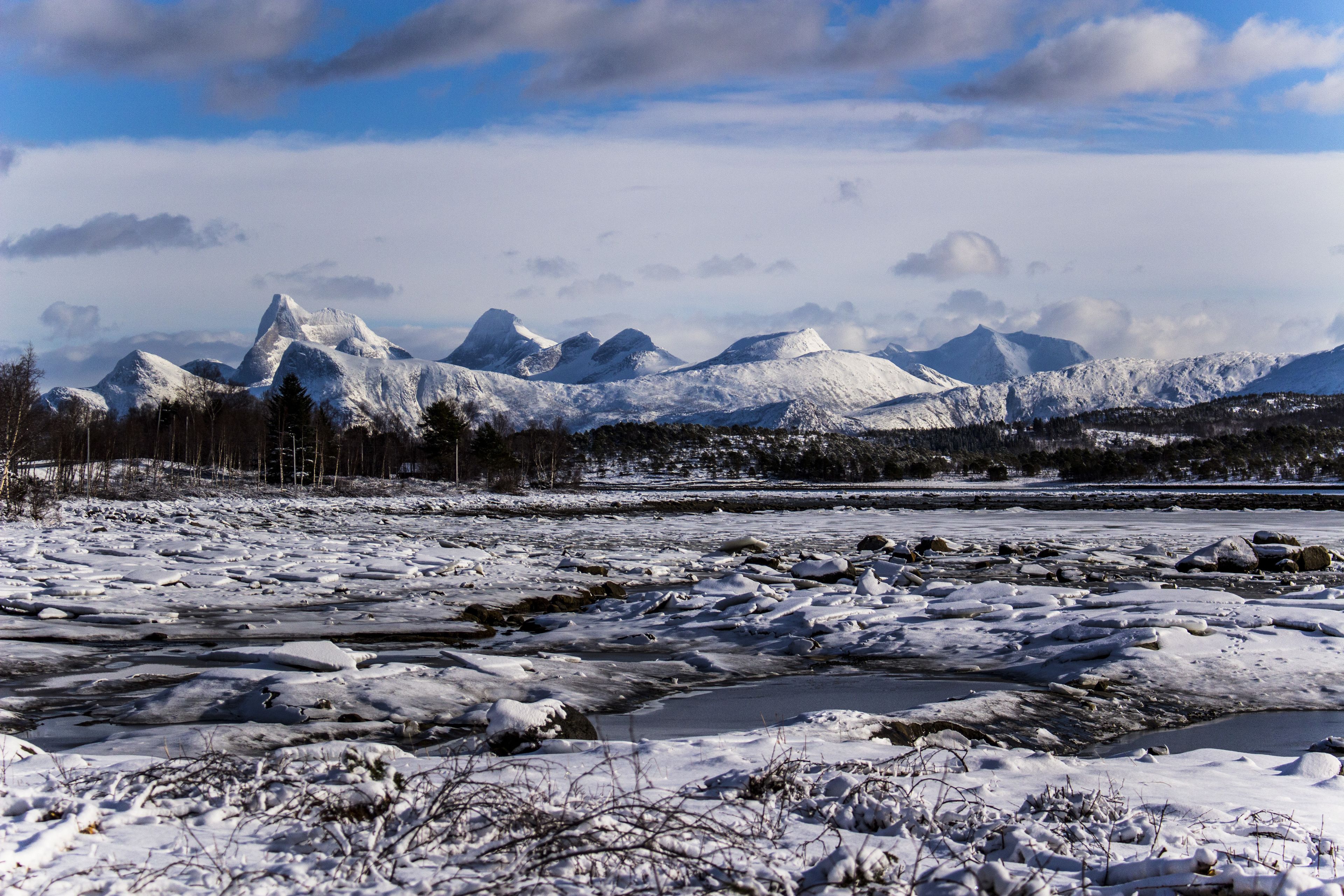Paisagem nevada com montanhas ao fundo e um rio congelado em primeiro plano.