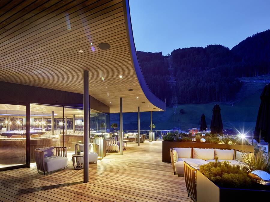 Un'area relax esterna moderna con pavimento in legno, zone salotto e vista su un paesaggio montano.