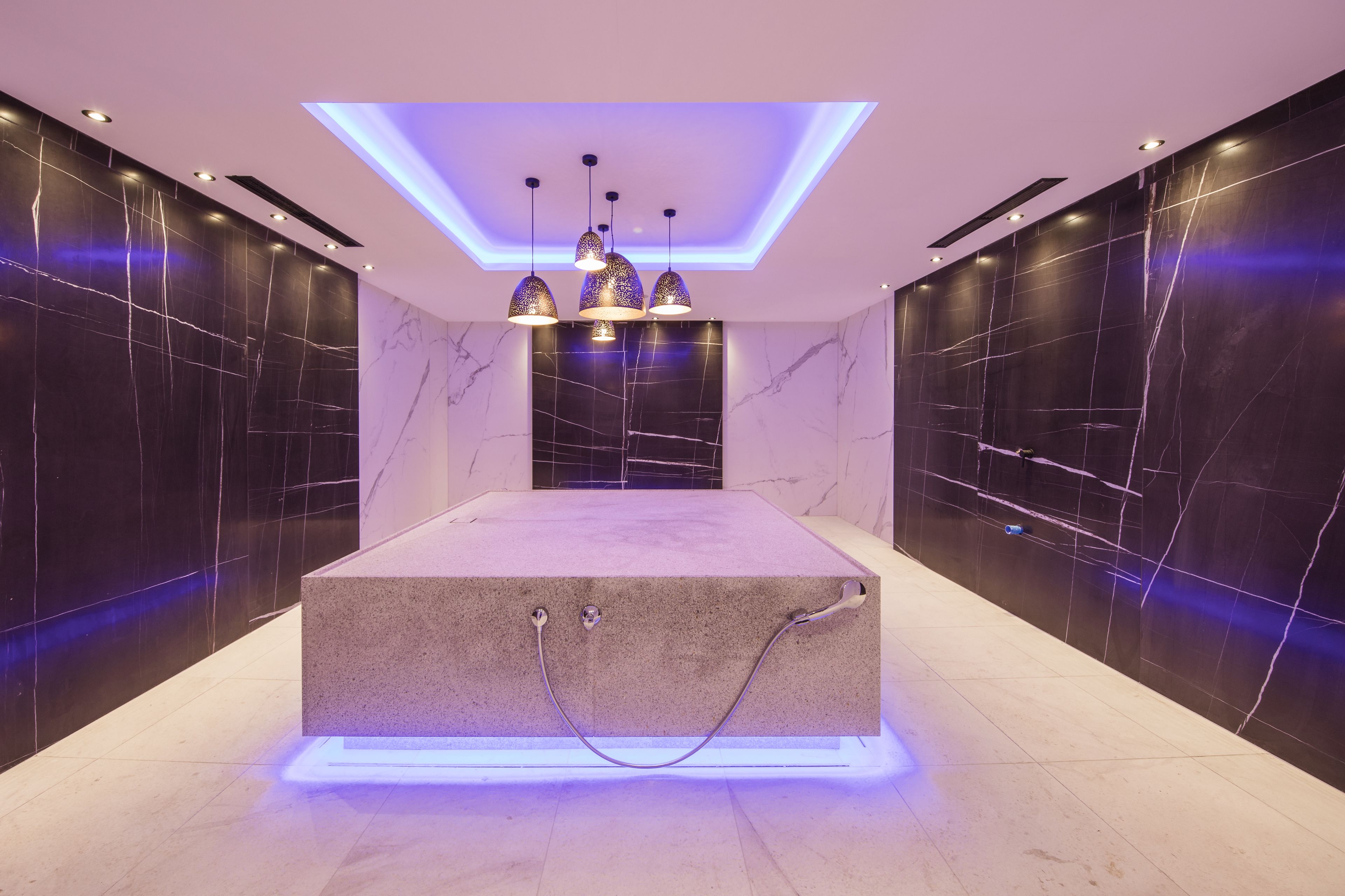A modern bathroom with a central rectangular platform, recessed lighting, and pendant lights.