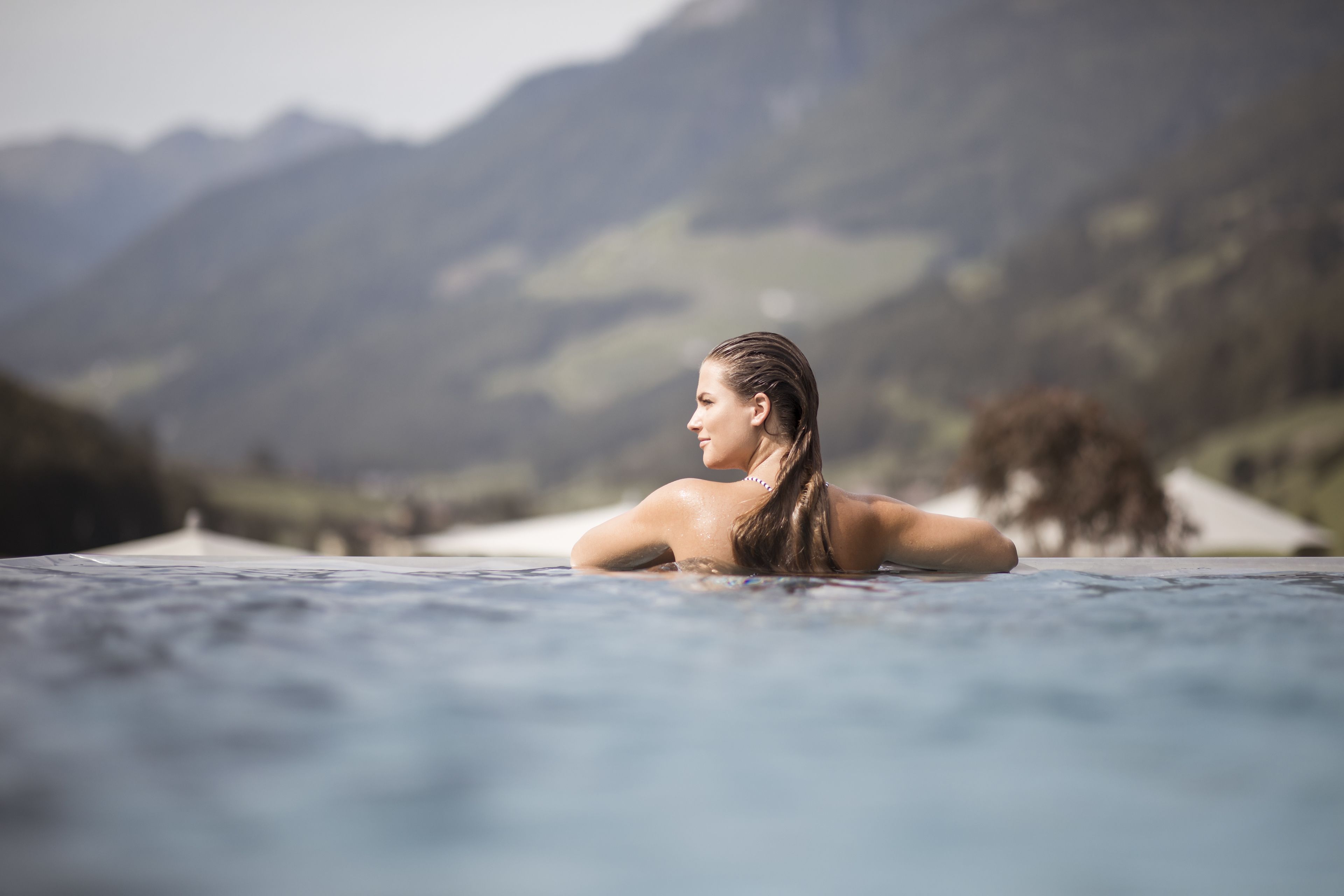 Eine Person in einer Whirlwanne vor einer gebirgigen Landschaft.