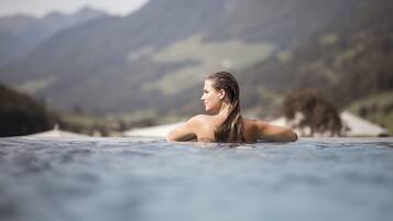 Eine Person in einer Whirlwanne vor einer gebirgigen Landschaft.