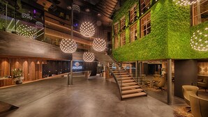 A spacious lobby with a wooden reception desk, a staircase, and a green wall with plants.