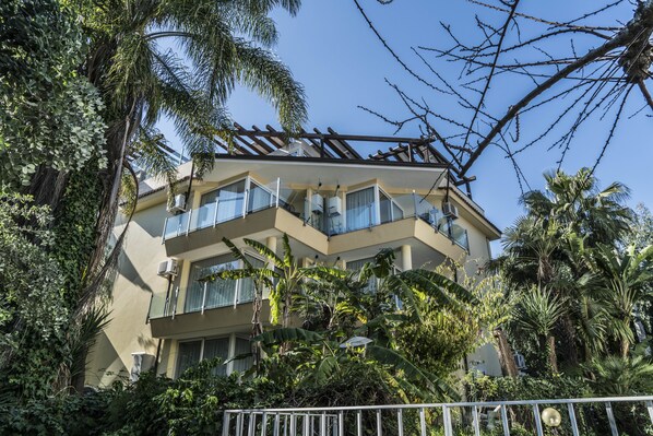 Un immeuble à plusieurs étages doté de balcons, entouré d’une végétation luxuriante et de palmiers.