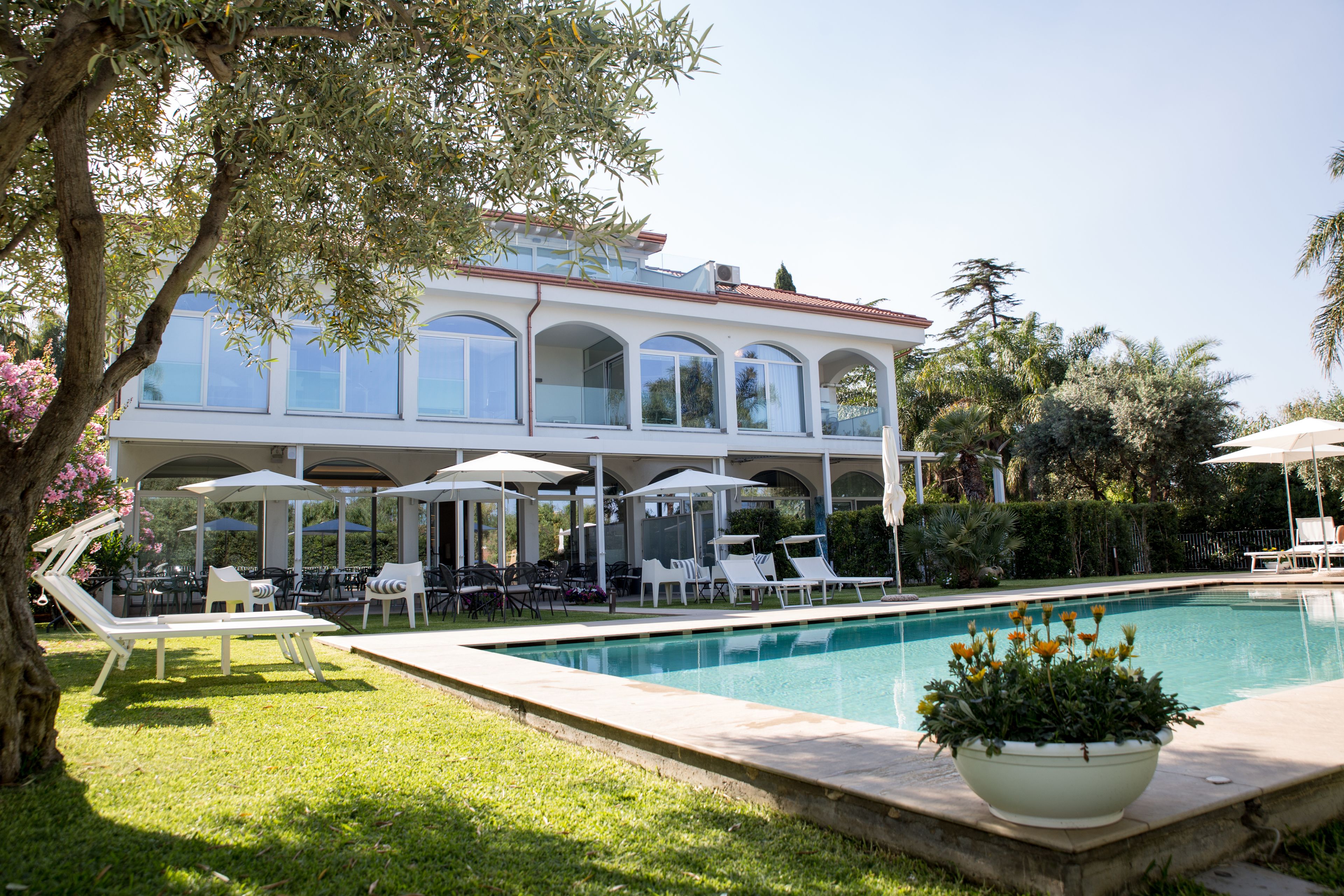 A poolside area with lounge chairs, umbrellas, and a large flower pot.