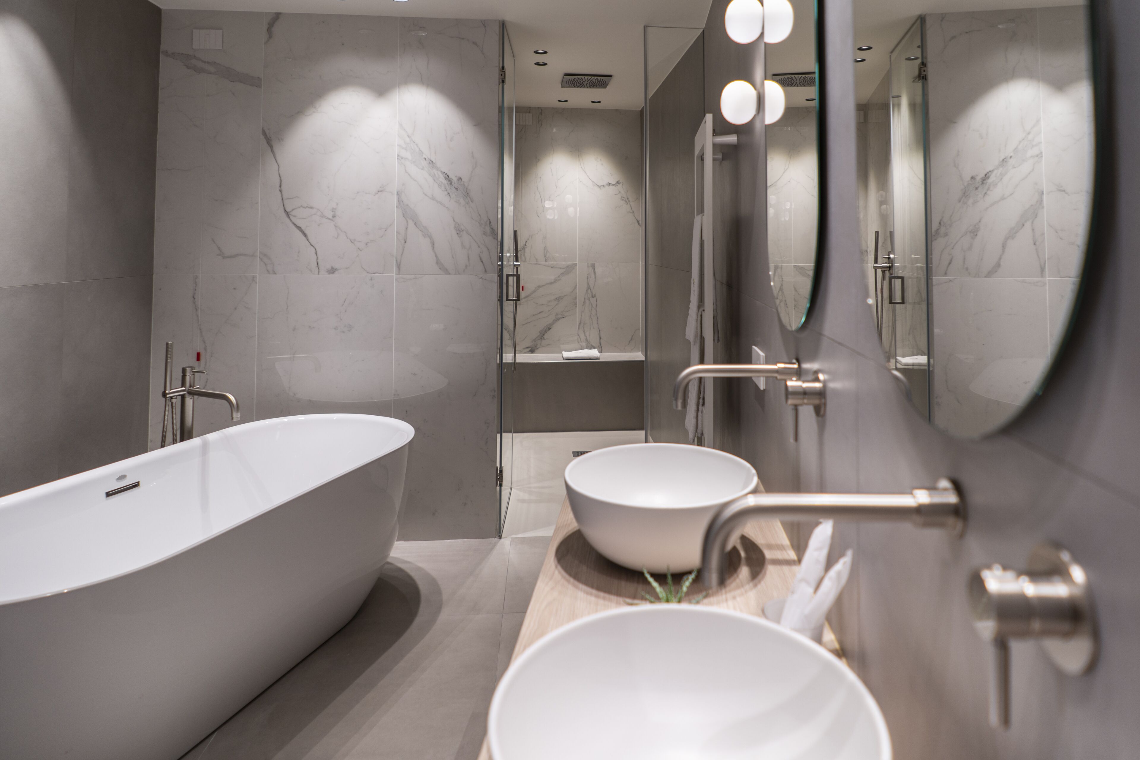 A modern bathroom with a freestanding bathtub, a large mirror, and a wooden vanity with two bowls.