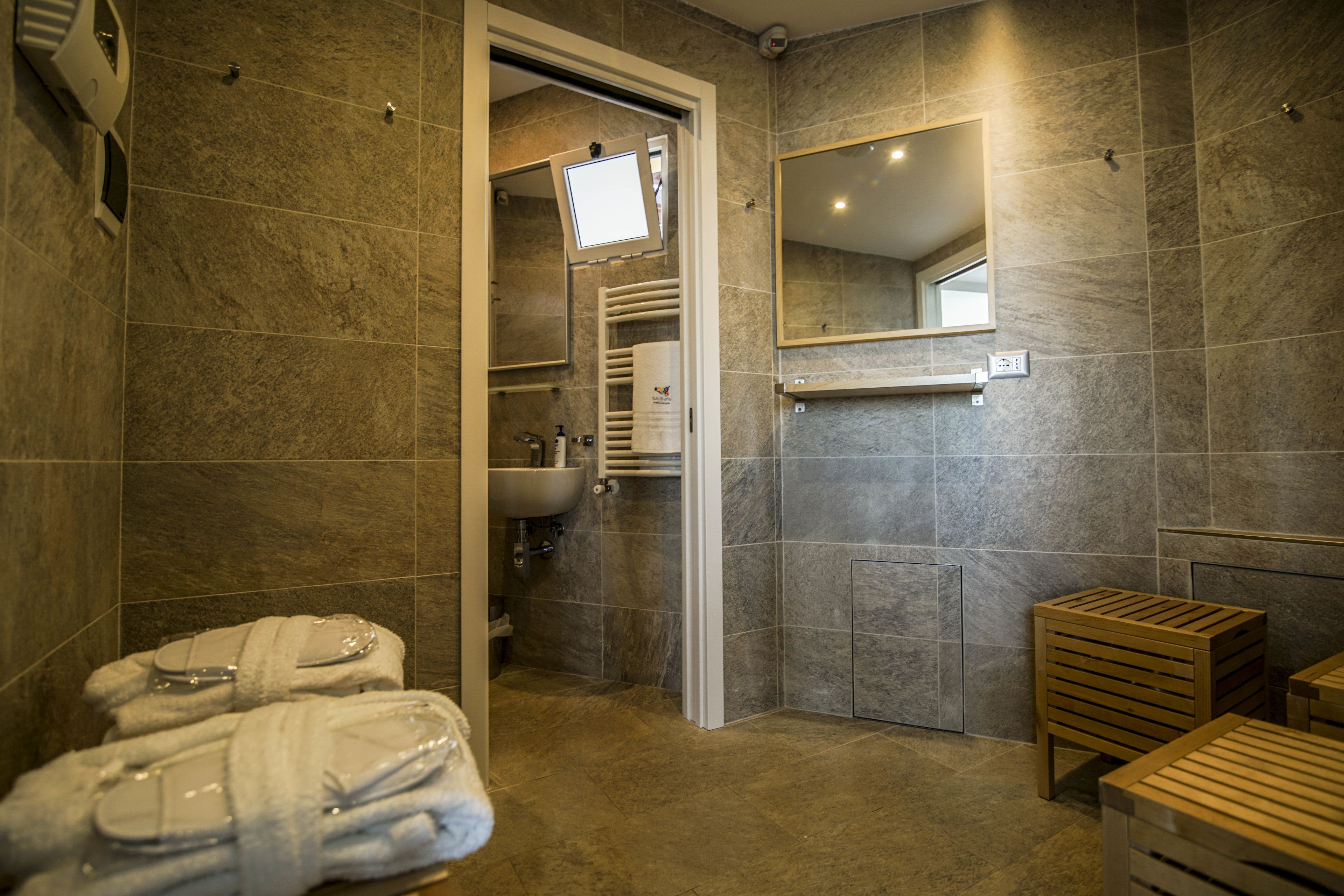 Ein modernes Badezimmer mit Dusche, Waschbecken und Spiegel. Handtücher und ein hölzerner Hocker sind ebenfalls vorhanden.