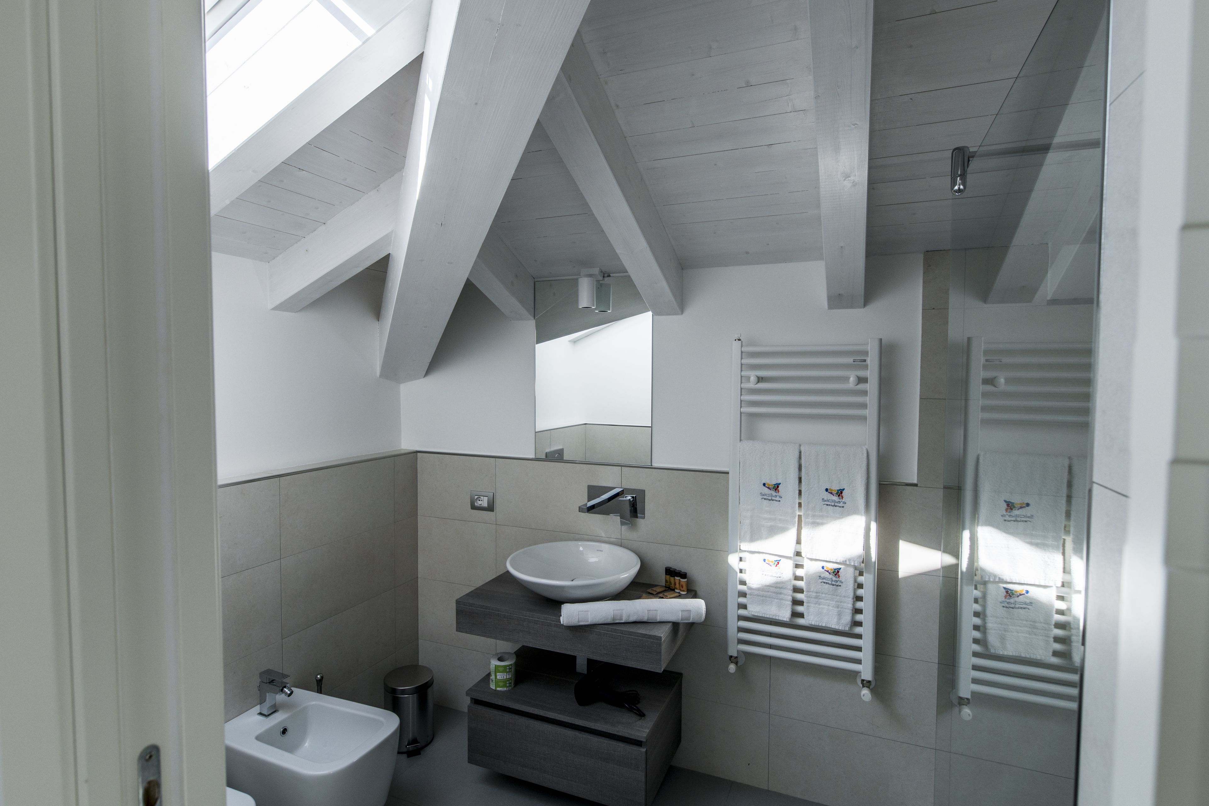 A modern bathroom with a skylight, a large sink, a vanity, and a towel rack.