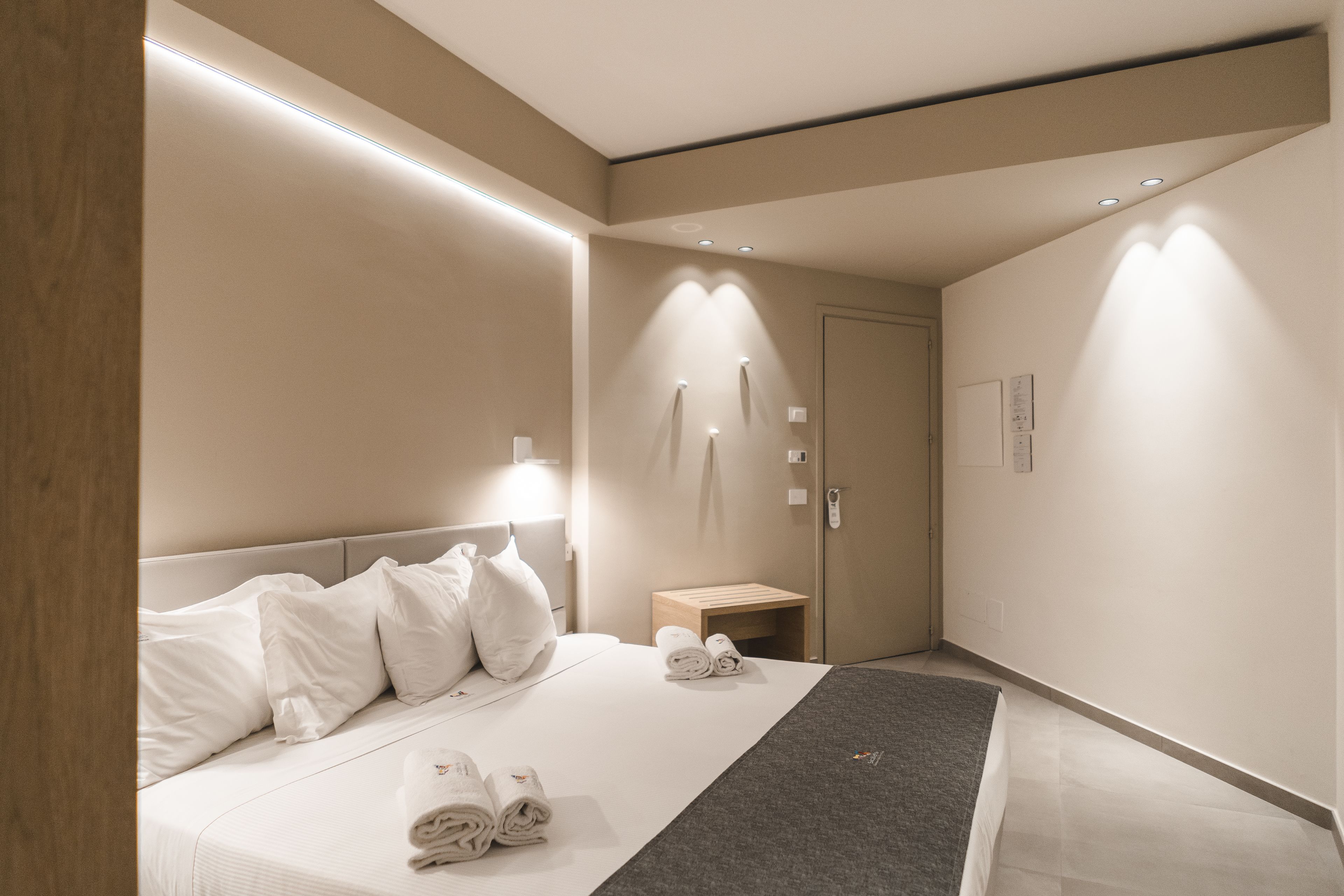 A modern hotel room with a neatly made bed, a small wooden side table, and a door with a keycard lock.