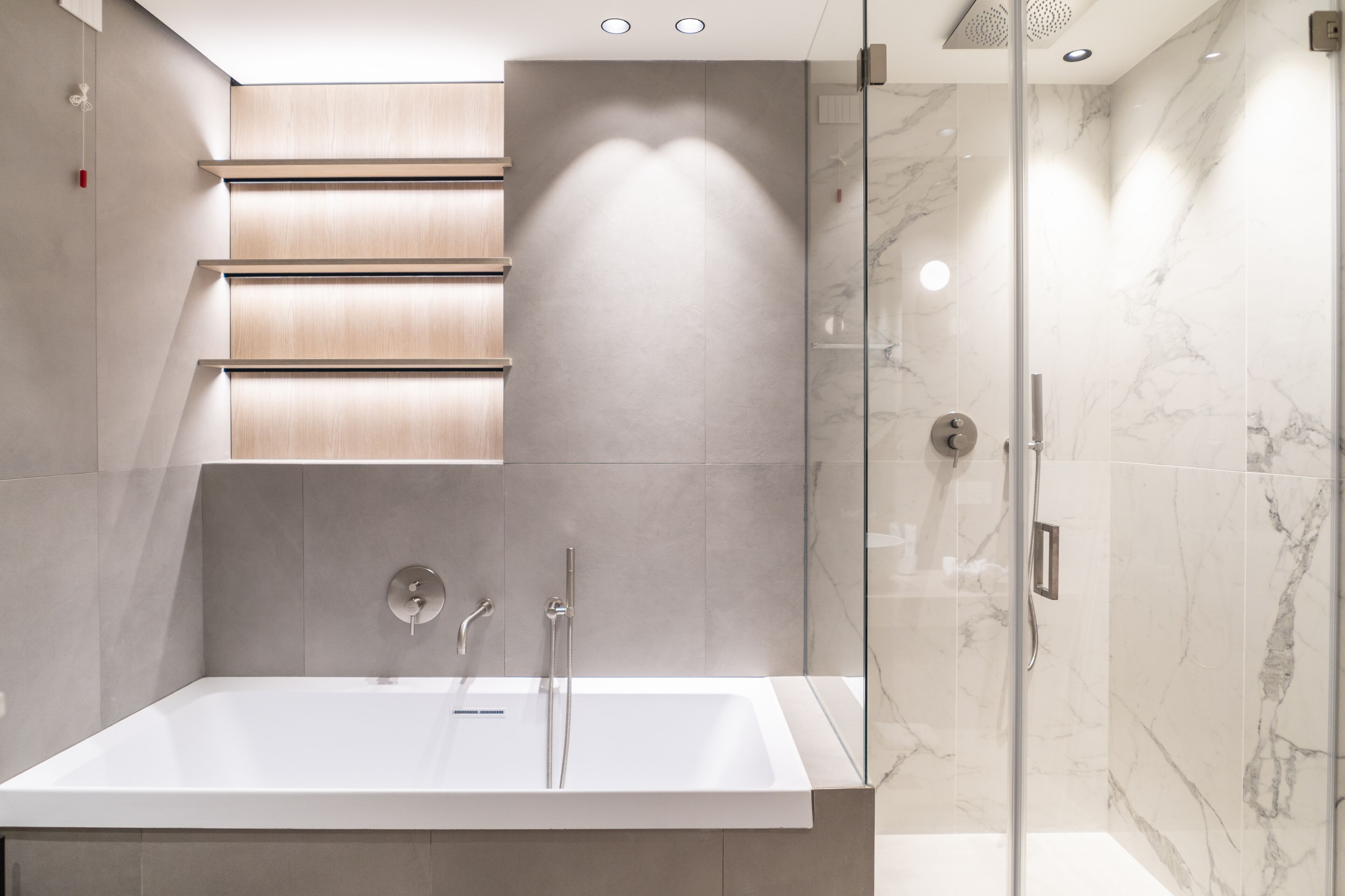 Ein modernes Badezimmer mit einer großen Badewanne, einer Duschkabine aus Glas und einem wandmontierten Waschtisch mit beleuchtetem Spiegel.