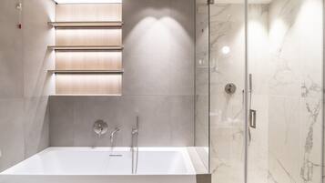 A modern bathroom with a large bathtub, a glass shower enclosure, and a wall-mounted vanity with a lighted mirror.