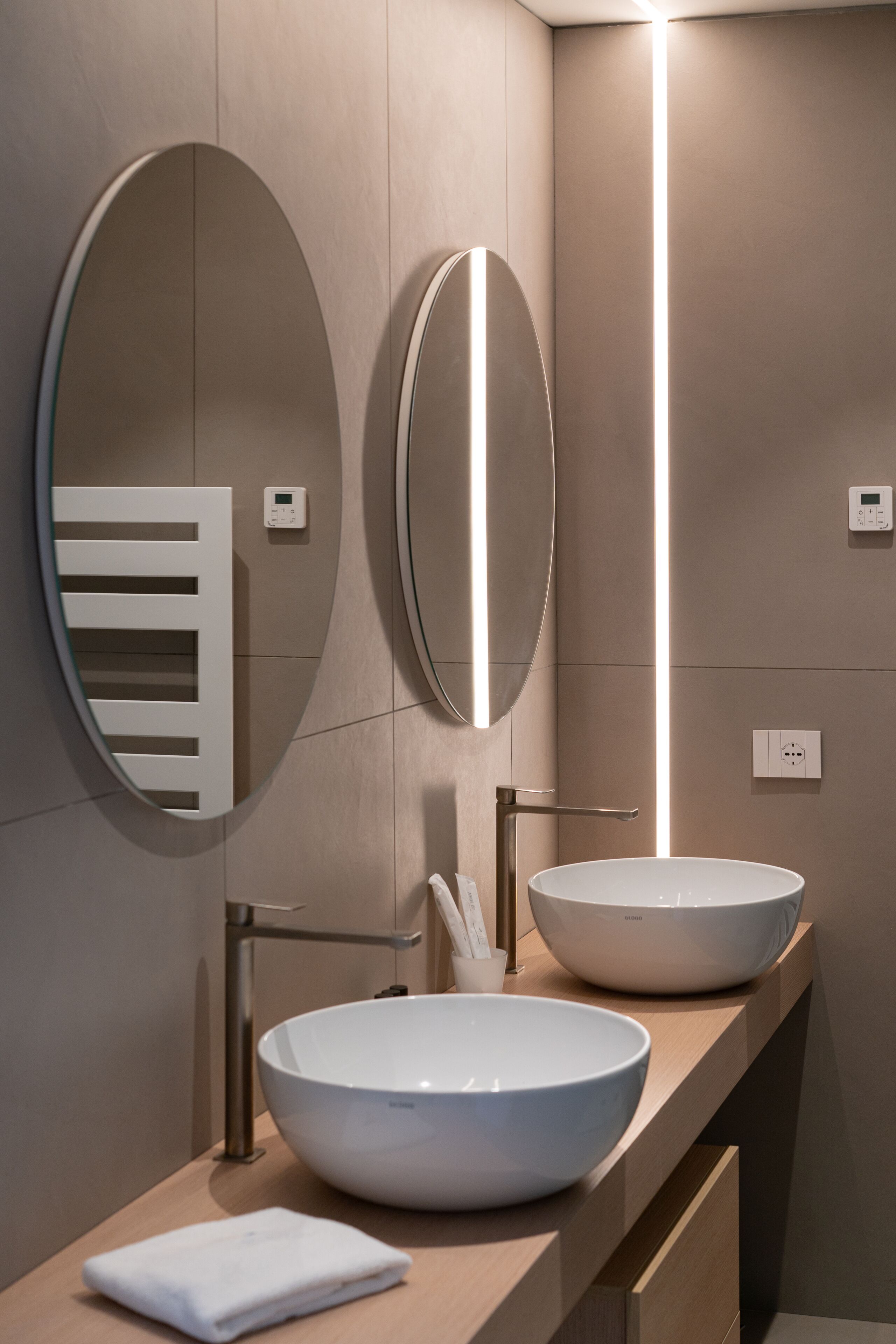 Een moderne badkamer met twee ovale spiegels, een wastafel en een handdoek op het aanrecht.