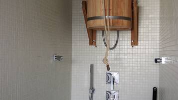 Zona de ducha con cabezal de ducha de cubo de madera, ducha de mano y grifo empotrado en la pared.