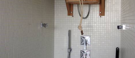 A shower area with a wooden bucket showerhead, a handheld showerhead, and a wall-mounted faucet.