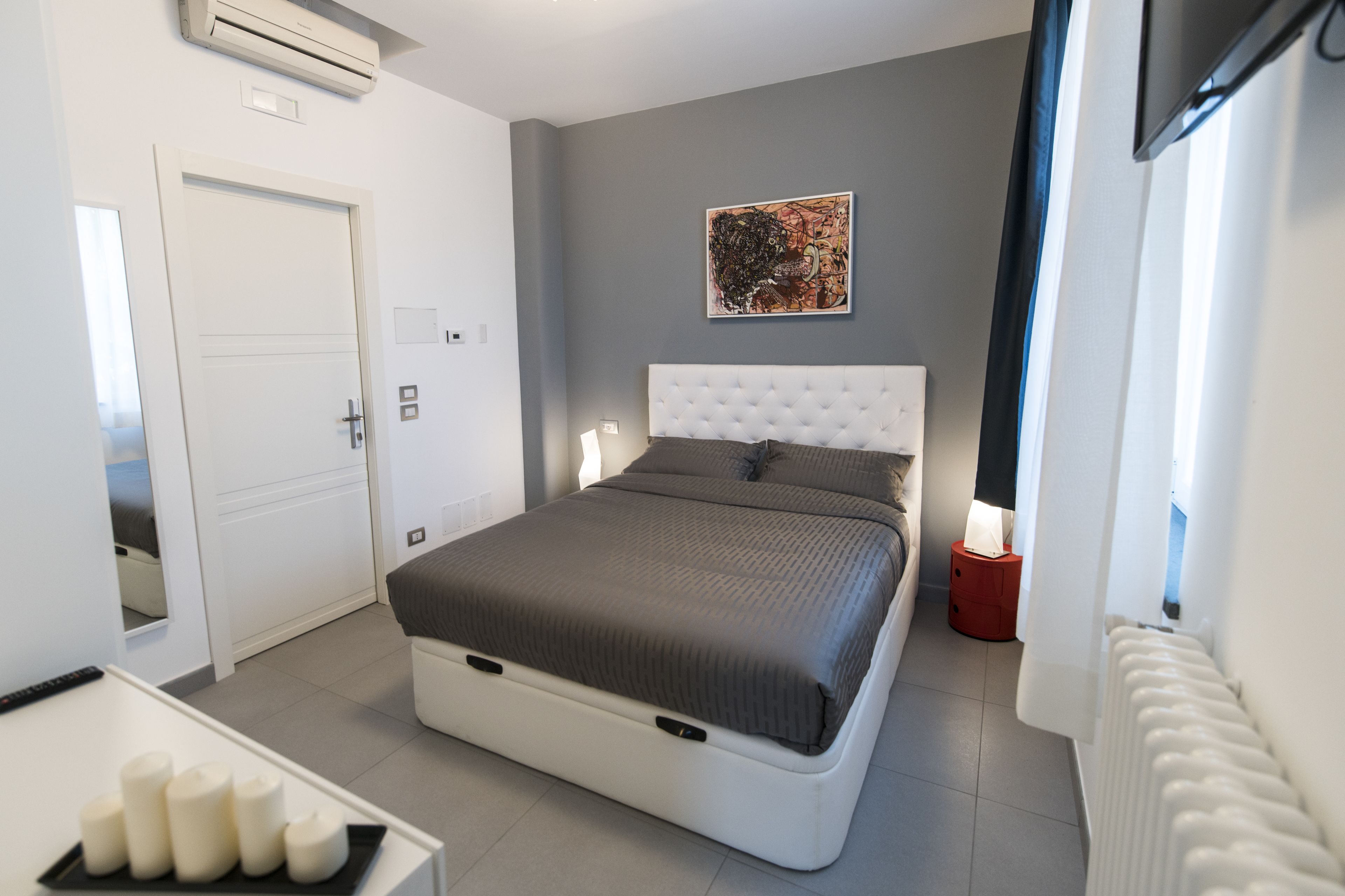 Une chambre moderne avec un grand lit, une tête de lit blanche, une table de chevet avec une lampe et un tableau au mur.