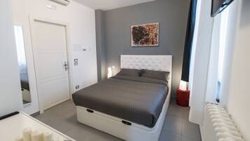 Une chambre moderne avec un grand lit, une tête de lit blanche, une table de chevet avec une lampe et un tableau au mur.