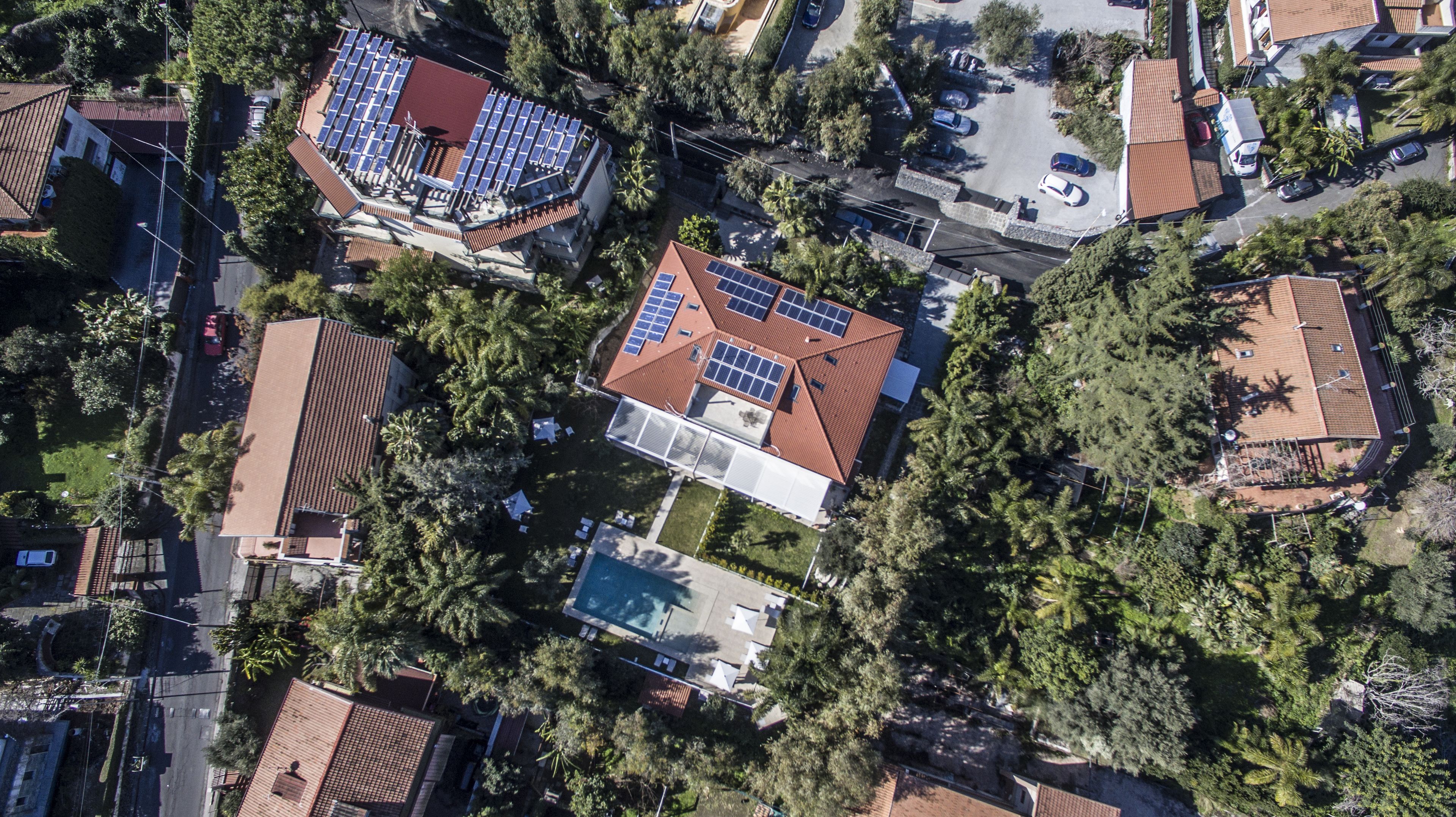 Vista aerea di una zona residenziale con case dotate di pannelli solari, alberi e una piscina.
