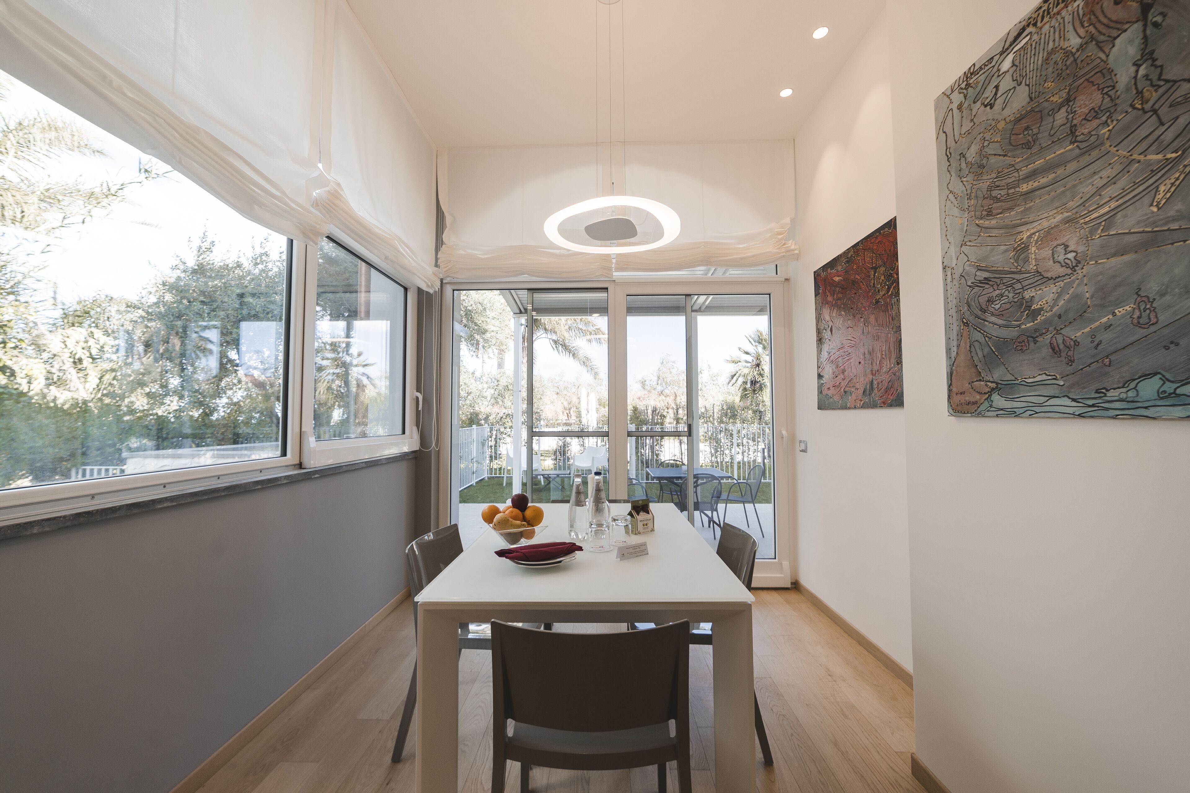 Un comedor moderno con una mesa blanca, sillas y vistas al exterior a través de amplios ventanales.