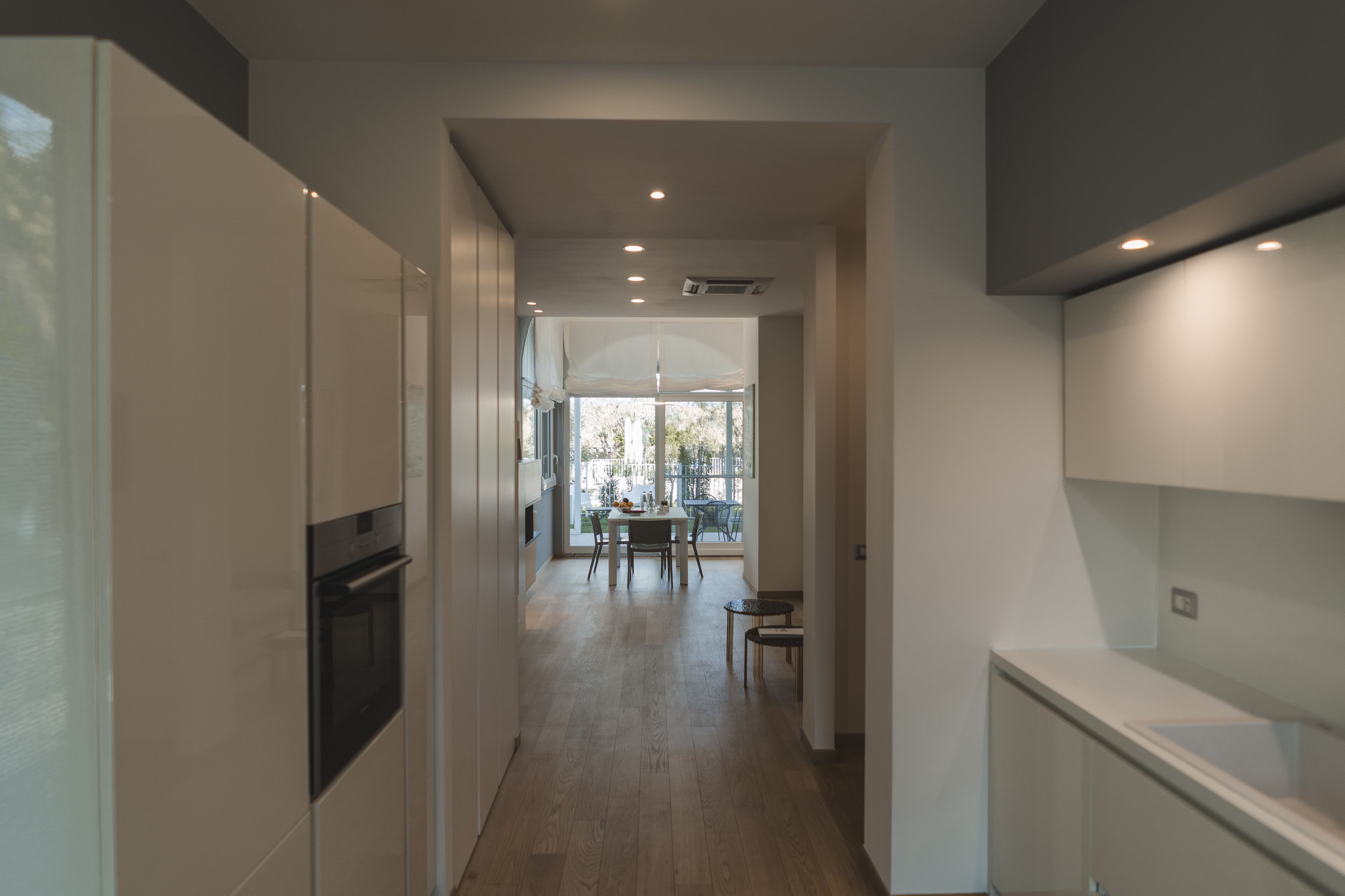 A modern kitchen with a built-in oven, a dining area with a table and chairs, and a view through a large window.