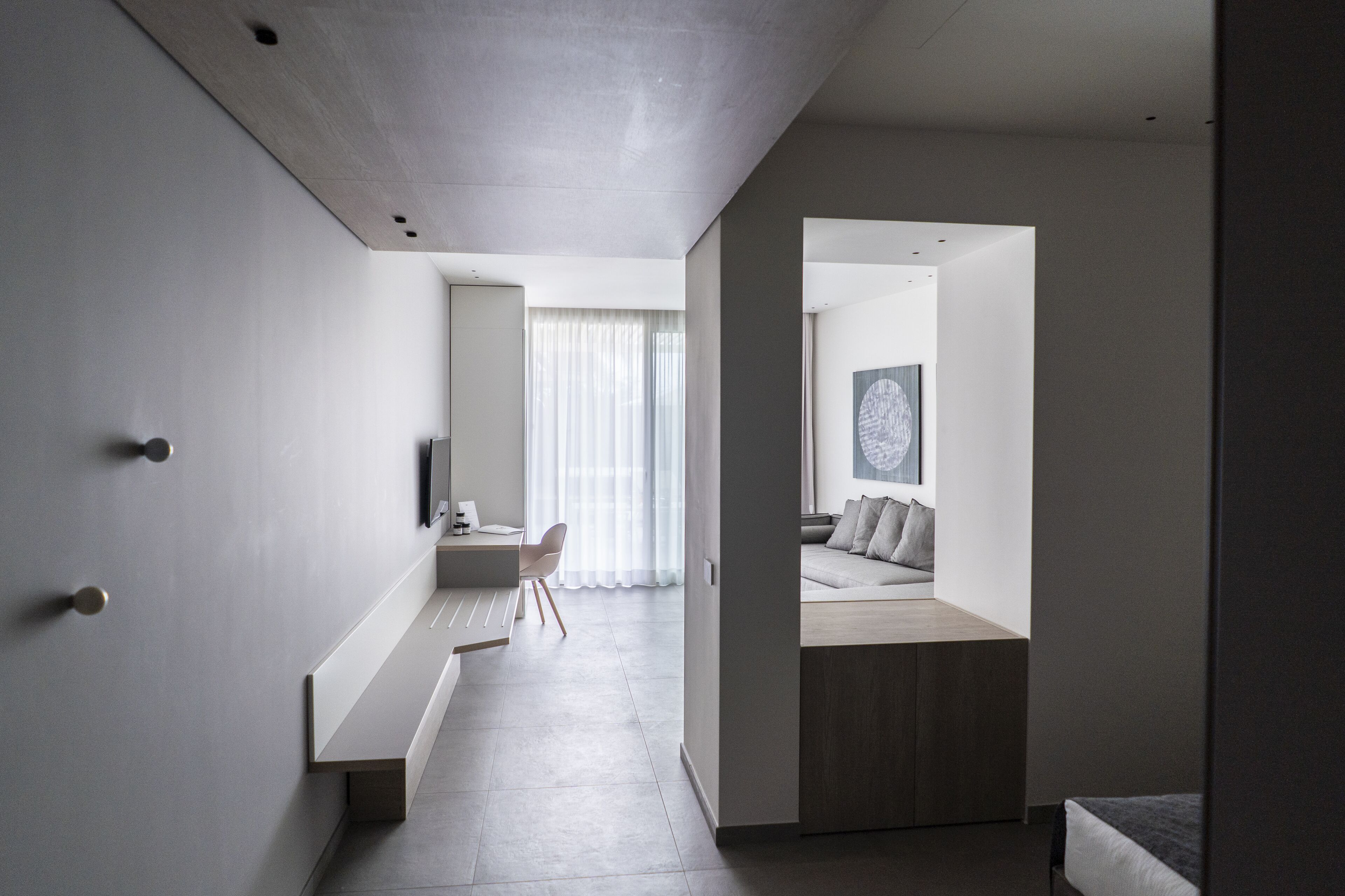 Habitación de hotel moderna y minimalista con un ventanal grande, un banco integrado y una zona de estar acogedora.