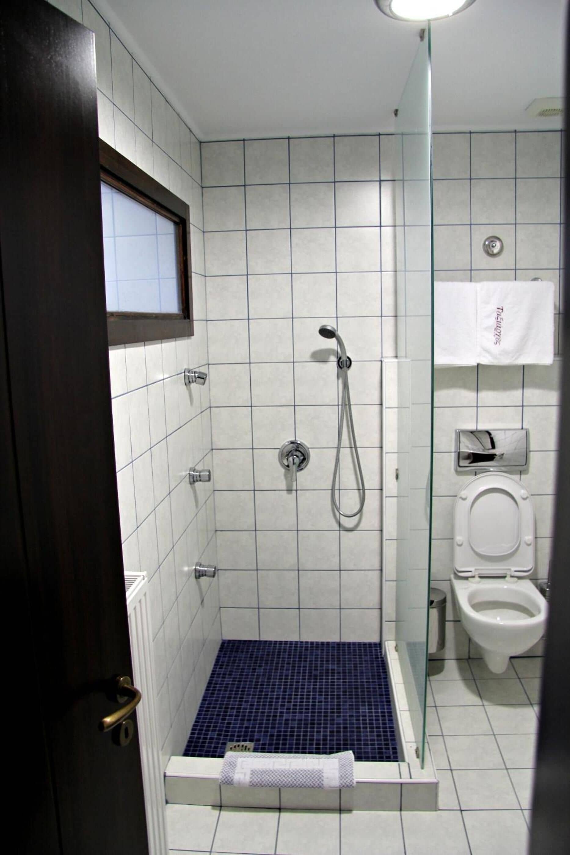 A small, tiled bathroom with a shower, toilet, and a window above the shower.