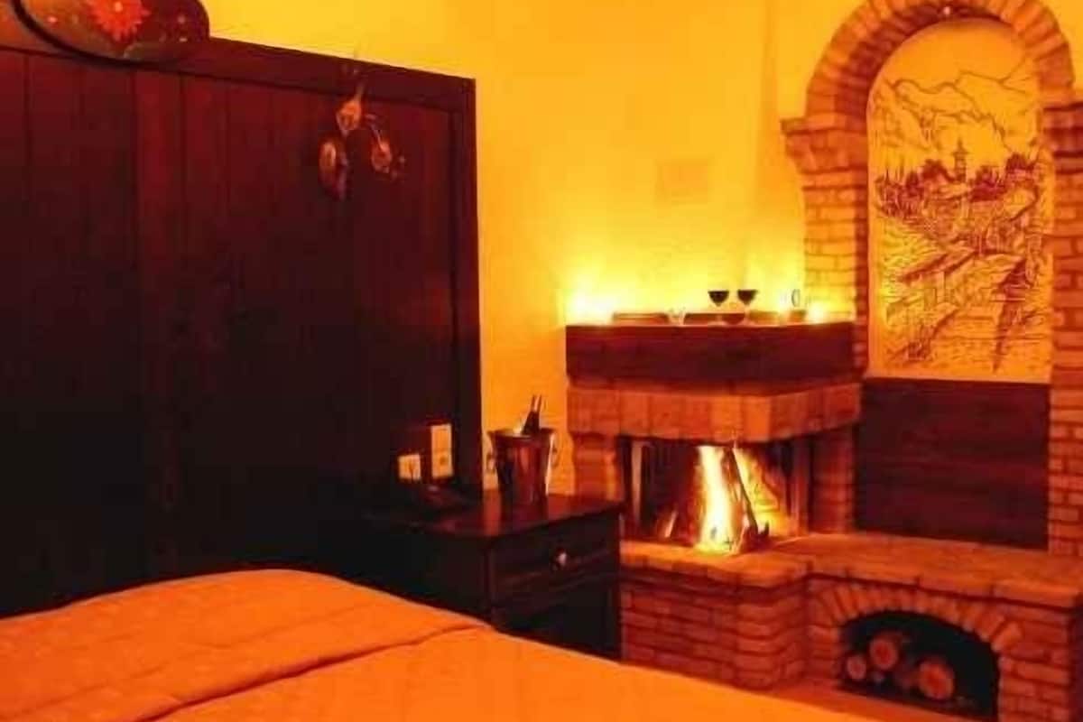 Une pièce comprenant un lit, une armoire en bois, une cheminée avec des bûches et un mur orné d’une fresque.