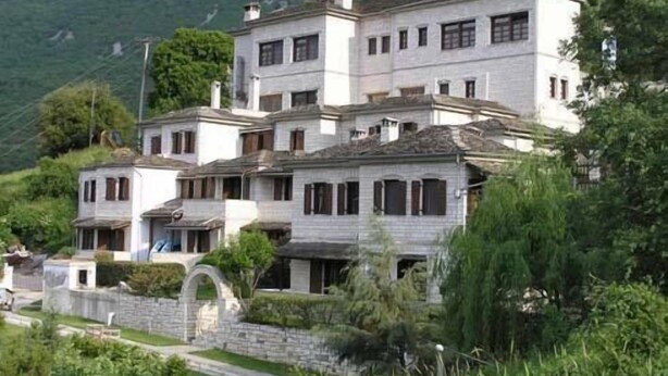 A multi-story building with a stone facade, multiple windows, and a stone pathway leading to the entrance. - Taxiarches Hotel (Zagori)
