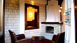 A cozy room with a fireplace, brick walls, and wooden furniture. - Taxiarches Hotel (Zagori)