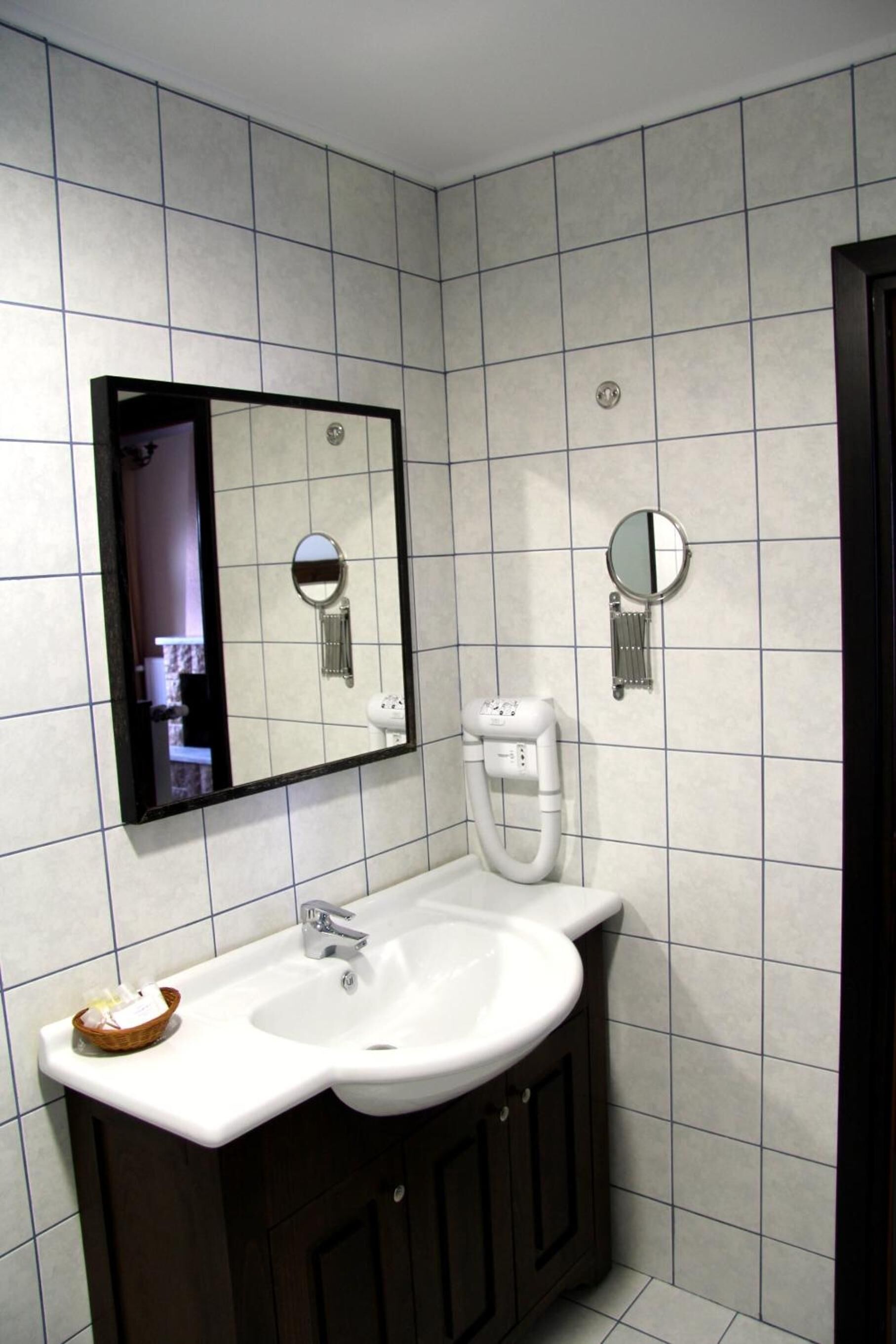 A bathroom with a white sink, dark wooden cabinets, a mirror, and a towel dispenser.