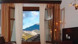 A hotel room with a large bed, a desk, and a view of a mountainous landscape through a window. - Taxiarches Hotel (Zagori)