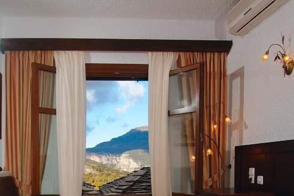 Une chambre d’hôtel avec un grand lit, un bureau et une vue sur un paysage montagneux, visible par la fenêtre.