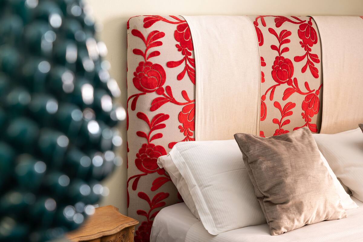Un lit avec une literie blanche et beige, une tête de lit à motifs floraux et un sapin de Noël en arrière-plan.