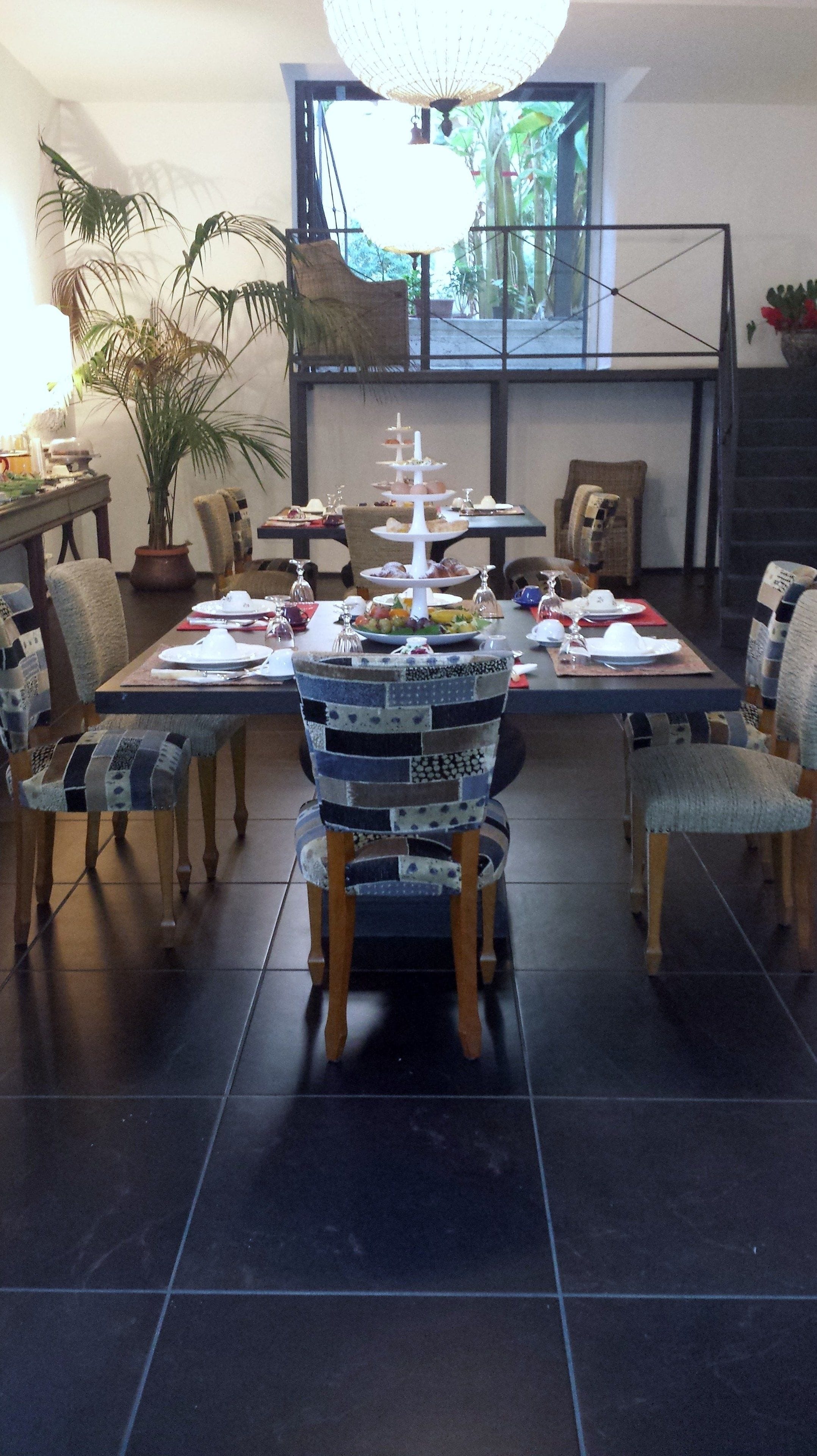 A dining area with a three-tiered dessert stand, a potted plant, and a large window with a view of greenery.