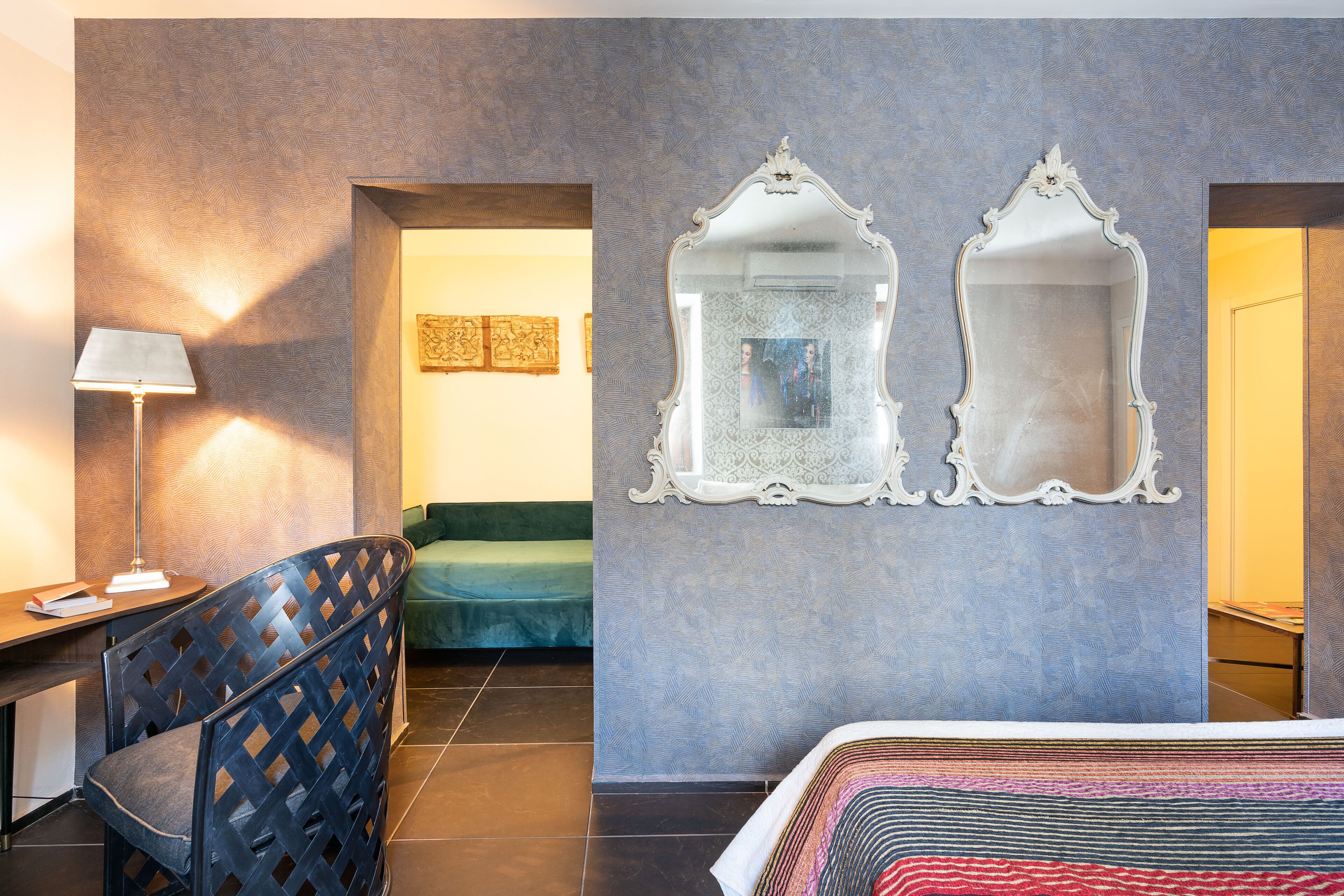 A hotel room with a bed, a desk, a chair, two wall mirrors, and a lamp.
