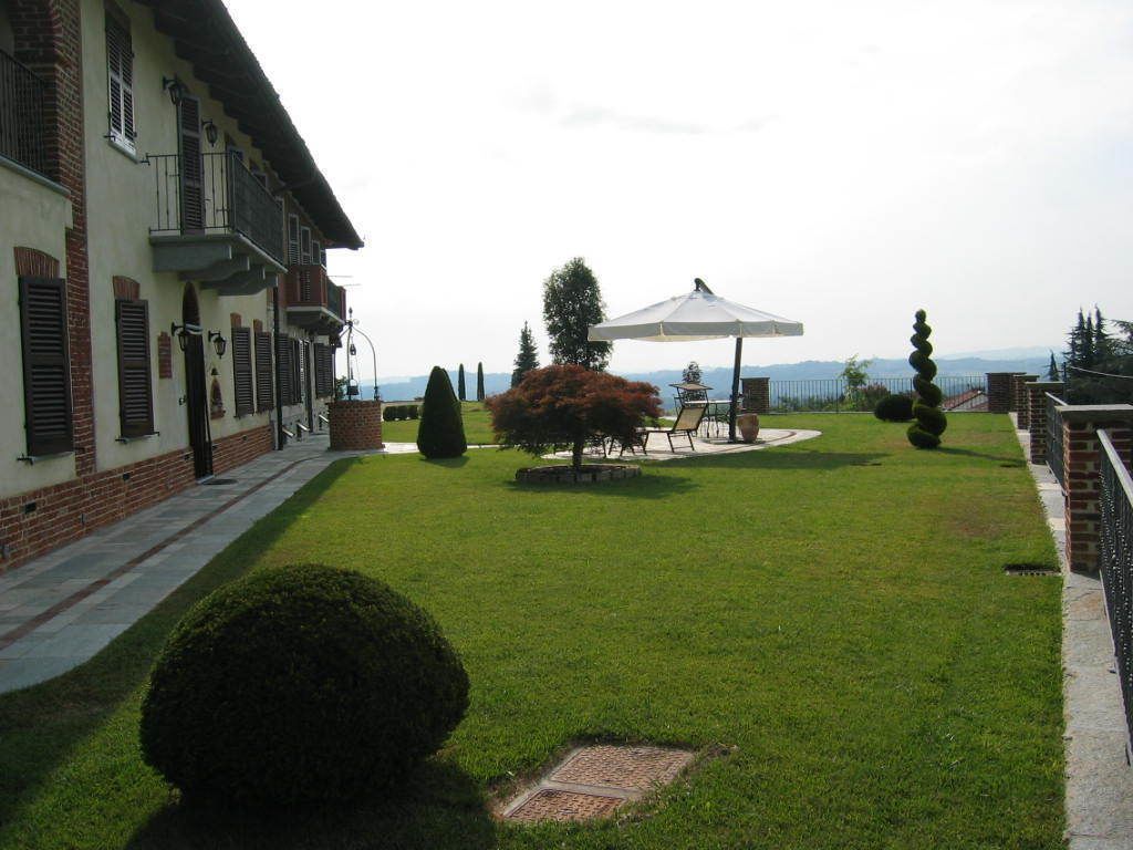 A well-maintained courtyard with a lawn, a seating area with a table and chairs, and a building with a balcony.