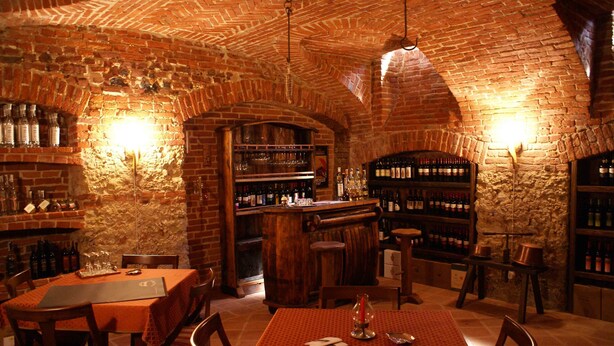 A brick-walled bar area with wooden tables and chairs, shelves with bottles, and a counter. - Cascina Bellavista (Tigliole)