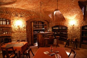 A brick-walled bar area with wooden tables and chairs, shelves with bottles, and a counter. - Cascina Bellavista (Tigliole)