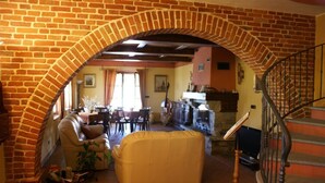 A cozy living room with a brick archway, a sofa, a dining area, and a staircase. - Cascina Bellavista (Tigliole)