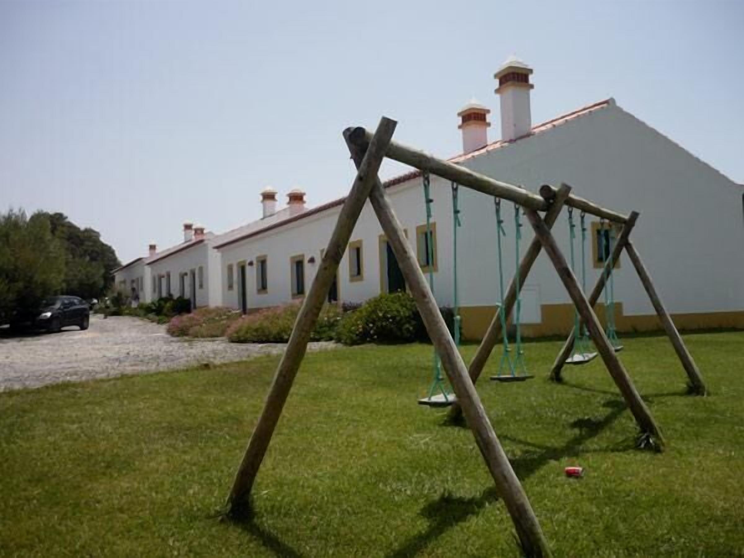 Un área verde con un columpio y un edificio blanco con varias chimeneas al fondo.