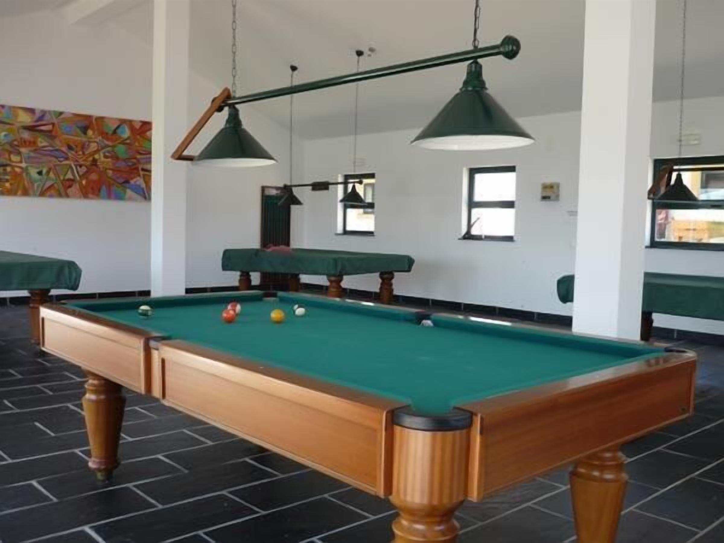 A pool table with a wooden frame and green felt, surrounded by black-tiled flooring and green cushioned seating.