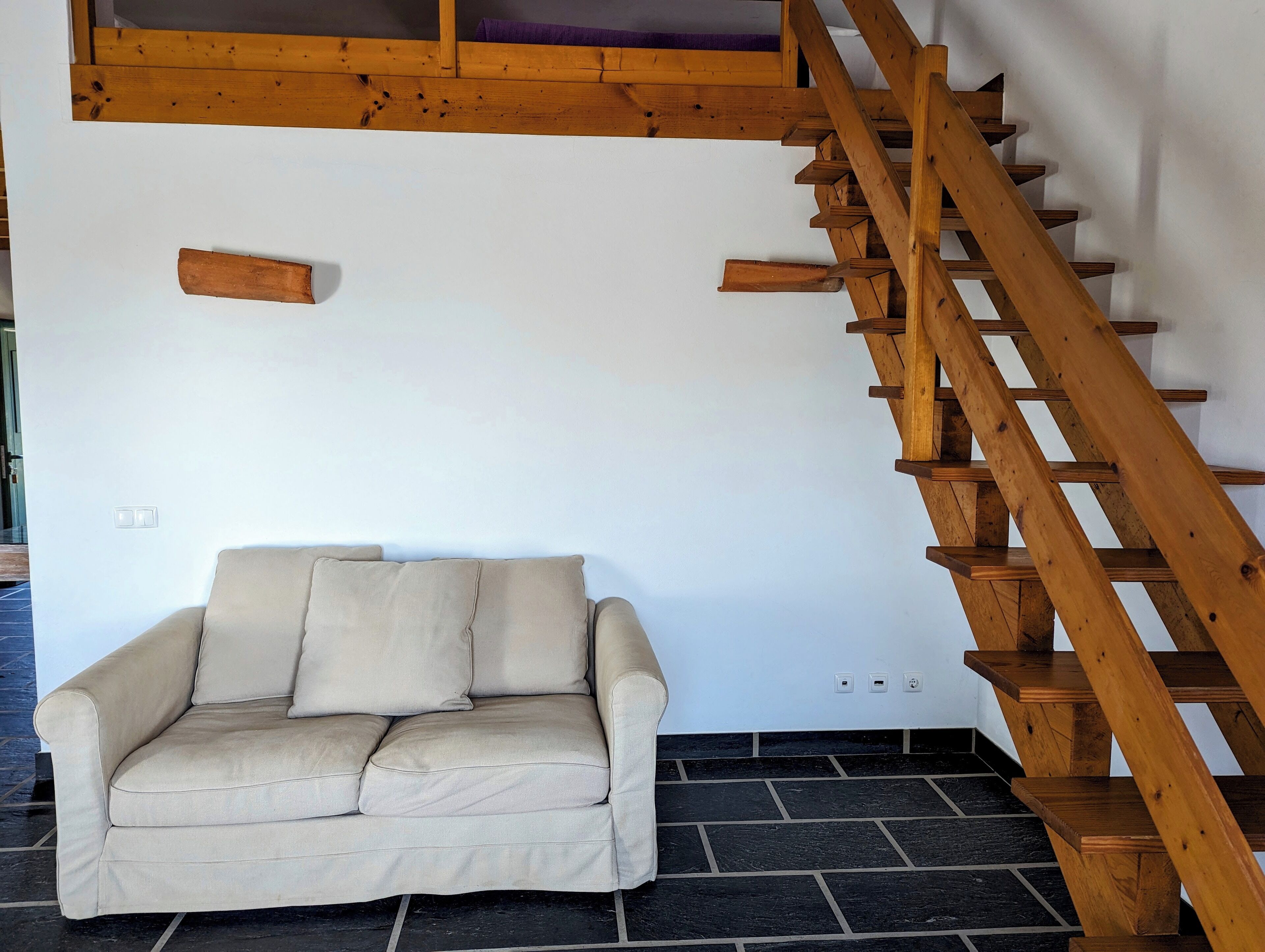 Una habitación con escalera de madera, sofá color crema y pared blanca.
