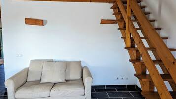 Una habitación con escalera de madera, sofá color crema y pared blanca.