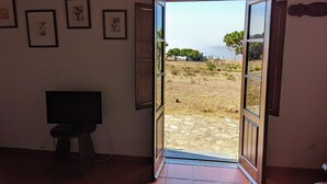 Una habitación con un televisor sobre un taburete, una puerta que da al exterior y cuadros en la pared.