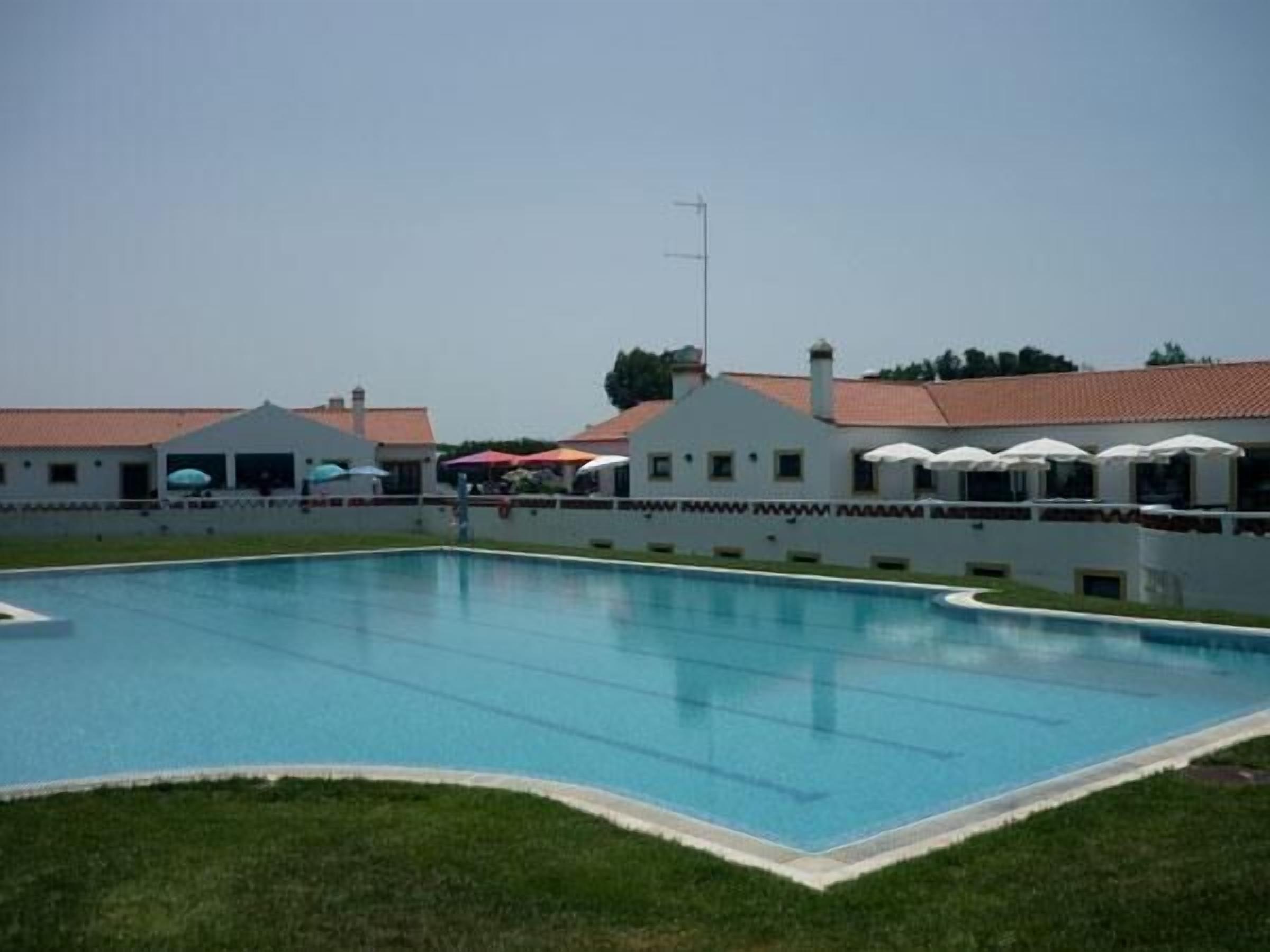 Una piscina con valla blanca y sombrillas, rodeada de edificios con tejados rojos.