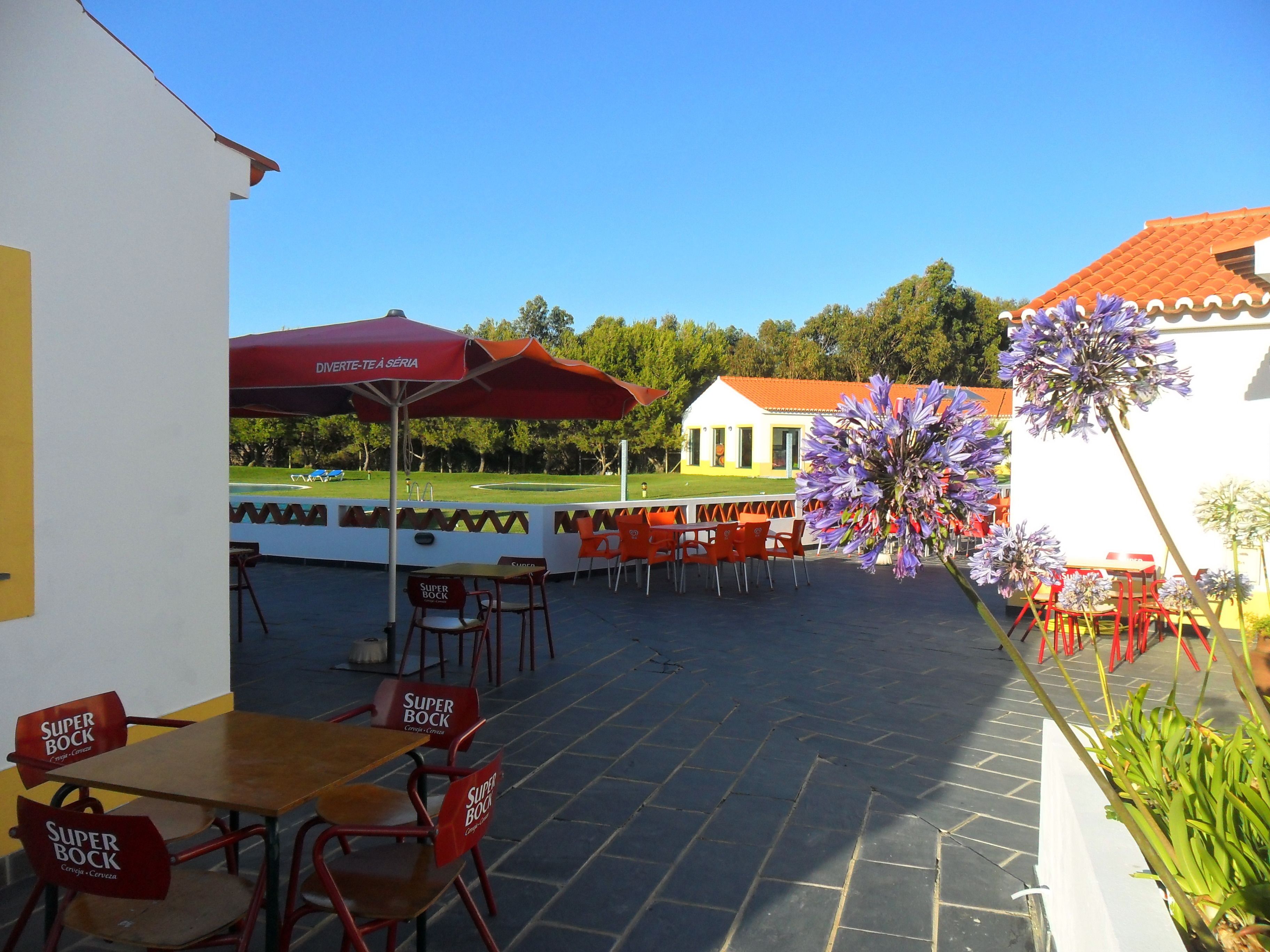 Un espace extérieur aménagé en terrasse, avec des tables et des chaises, un parasol rouge et une vue sur un terrain de golf.