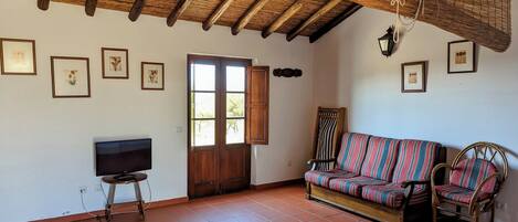 A spacious living room with a wooden ceiling, a sofa, two chairs, a television, and a door with a window.