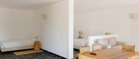Quarto de hotel moderno com sofá, mesa de jantar de madeira com cadeiras e uma pequena mesa de cabeceira com abajur.