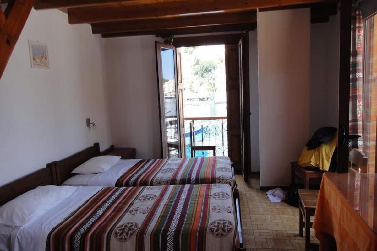 Quarto com duas camas, teto de madeira, uma mesinha e vista para uma varanda.