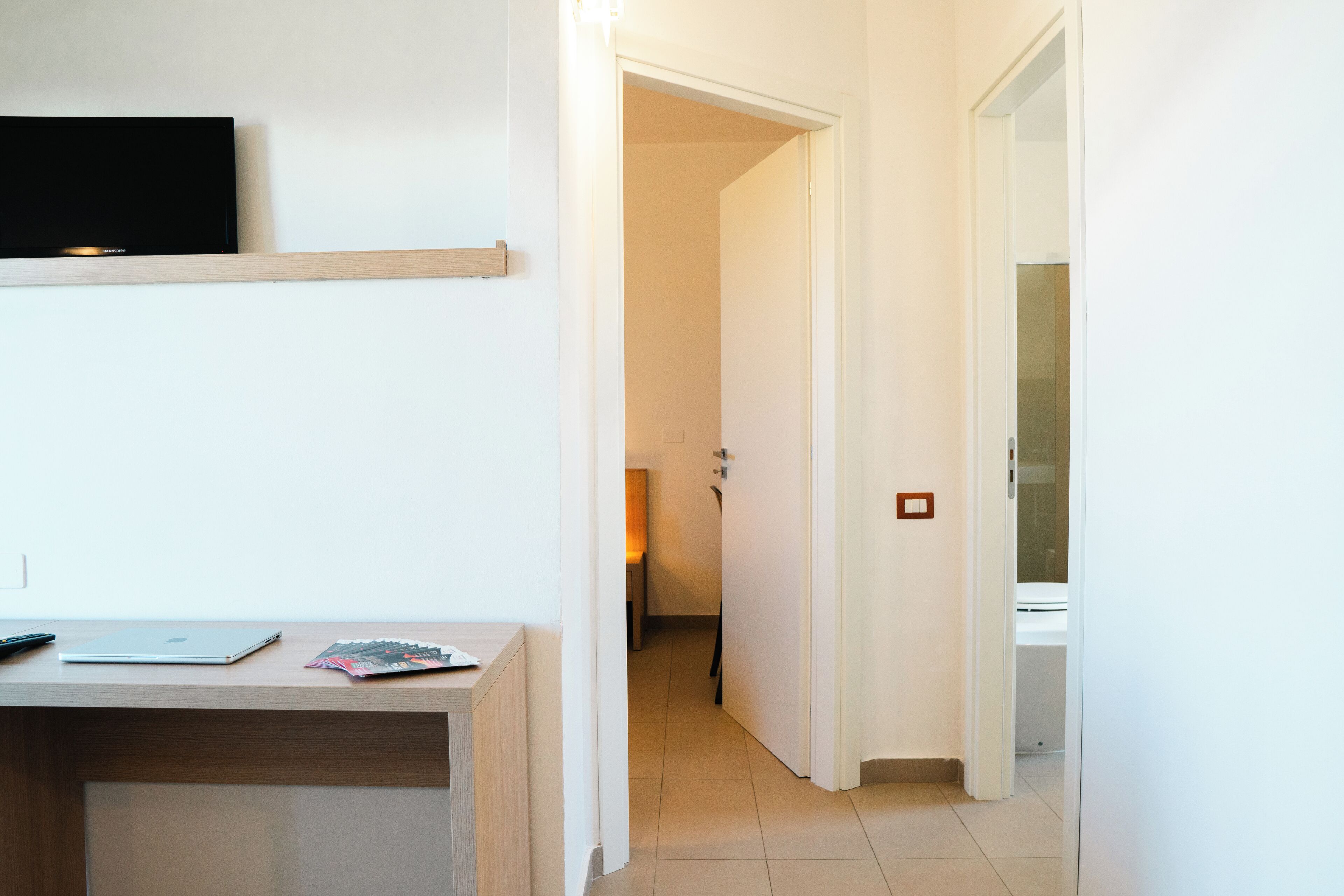 A clean, modern room with a desk, a flat-screen TV, and a door leading to another room.